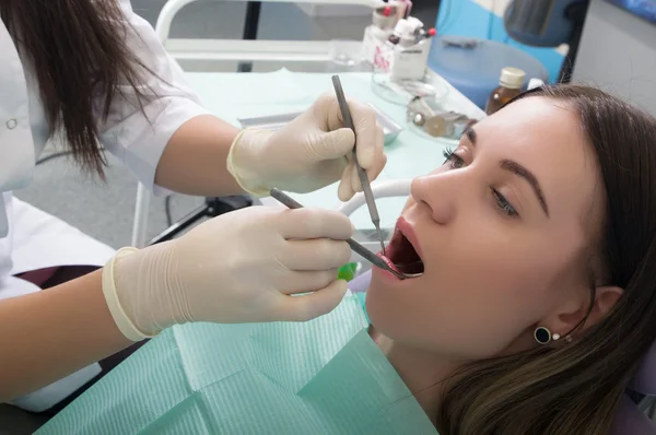 Mujer joven visitando dentista en clínica estomatológica. El médico examina la cavidad oral en la caries dental . — Foto de Stock