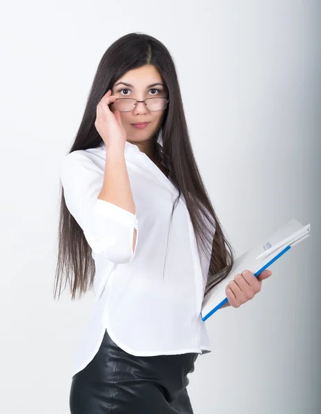 Eine junge, ziemlich schlanke Asiatin in weißer Bluse, schwarzem Lederrock und Brille, die einen Ordner mit Dokumenten in der Hand hält — Stockfoto