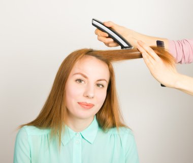Beautiful young red-haired girl at the hairdresser makes blow drying, shorn bangs, hair polishing