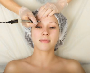 Beautician examining the face of a young female client at spa salon. Permanent makeup, tattoo in a beauty salon. Professional consultation