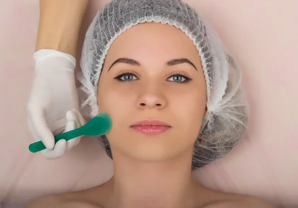 Kozmetikus megvizsgálja az arcát egy fiatal női ügyfél a spa szalon. kozmetikus csinál kozmetikai maszk, a beteg arca. Szakmai konzultáció — Stock Fotó