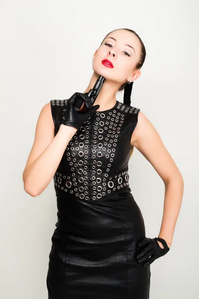 Jovem mulher sexy em vestido de couro preto com cabelo trançado está segurando uma arma — Fotografia de Stock