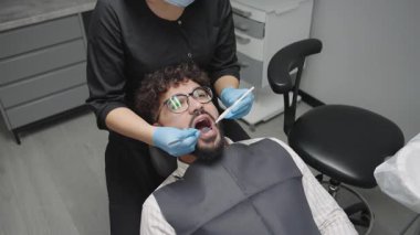 Modern bir klinikte dişçi muayenesi bir adamın profesyonel bir doktordan tedavi gördüğünü gösteriyor.