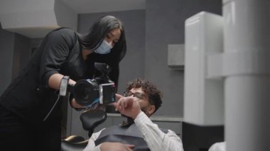 Diş hekimi, klinikteki hastalara uygulamaları yavaş çekimde alet ve tekniklerini gösterirken açıklıyor