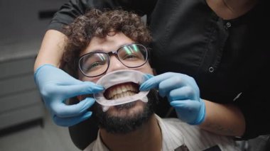 Dişçi, modern bir klinikte dişçi muayenesinde hastaya yavaş çekimde yardım ediyor.