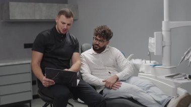 Dişçi, modern diş sağlığı kliniği ortamındaki hastalara tedavi seçeneklerini açıklıyor