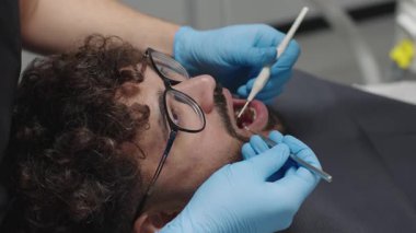 Dişçi modern klinikte rutin kontroller sırasında hastaların ağzını aletlerle muayene eder.