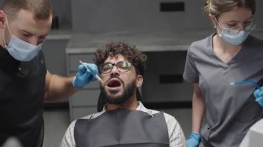 Diş hekimi, klinik ortamındaki hastalara rutin kontroller yapar. Temiz diş prosedürleri ve takım çalışması sergiler.