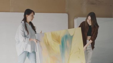Stüdyo ortamında renkli bir tablo sergileyen iki kadın arasındaki sanatsal işbirliği