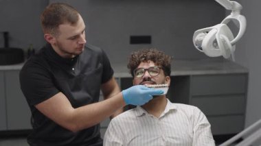 Diş hekimi, dişçi muayenehanesindeki bir hastanın dişlerini aletlerle ve aletlerle kontrol eder.