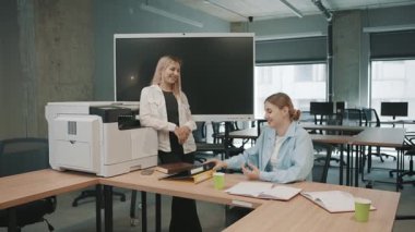 Meslektaşlar ofis projelerini modern bir çalışma alanında yazıcı kullanırken ve belgeleri incelerken tartışırlar