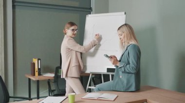 Çalışma saatleri boyunca çalışma odasındaki iki kadın ve sunum panosundaki çizelgeler arasındaki iş tartışması