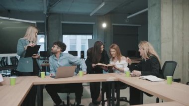 Modern bir ofiste, fikir alışverişi yapan ve gündüz vakti bilgi paylaşan bir grup ile iş toplantısı yapılıyor.