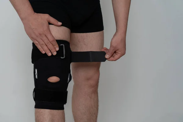 Leg support. A man adjusts a black orthosis on his leg. Copspace.