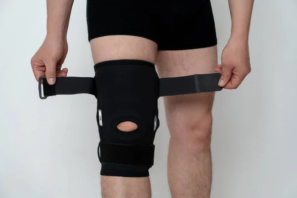 Leg support. A man adjusts a black orthosis on his leg. Copspace.