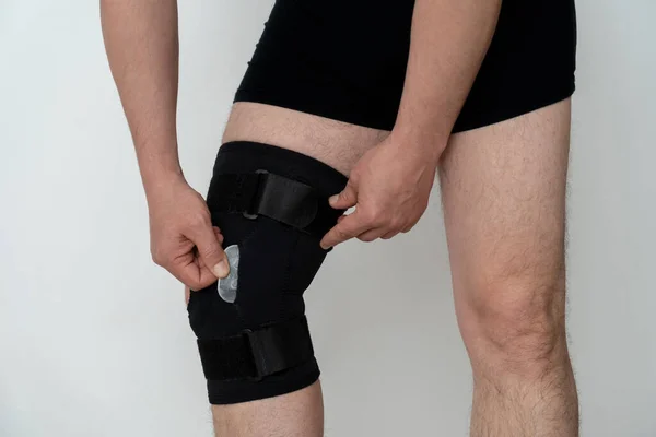 Leg support. A man adjusts a black orthosis on his leg. Copspace.