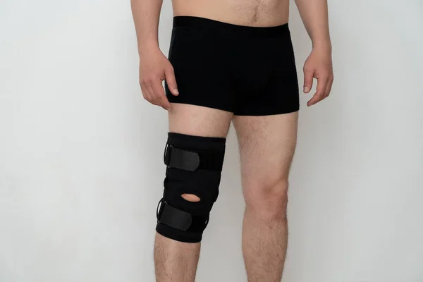 Leg support. A man adjusts a black orthosis on his leg. Copspace.