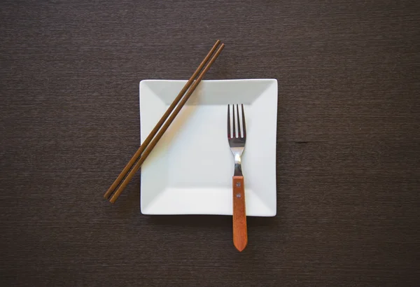 フォークと箸の木製テーブルと空の白いプレート — ストック写真