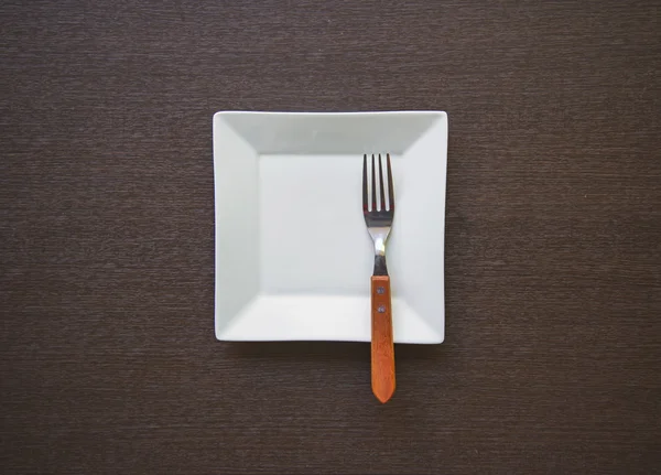 木製のテーブルにフォークを持つ空の白いプレート — ストック写真