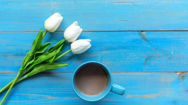 Kış sıcacık geçiyor. Güneşli bir günde mavi ahşap arka planda zambak çiçeği yazan bir fincan sıcak kahve. Yaşam tarzı kavramı