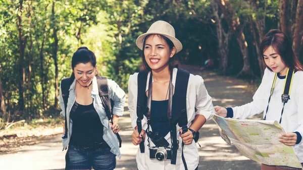 Group women traveler with backpack adventure holding map to find directions and walking relax in the jungle forest outdoor for destination leisure education nature on vacation. Travel and Lifestyle Concept