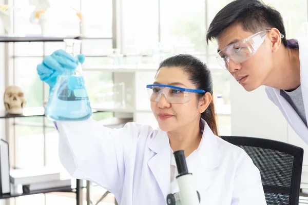 Team work asian woman and man Scientists analyzing study data and evaluating microscope success for work shop. Health care researchers doing some research with dropper chemical testing in life science laboratory