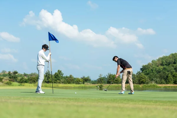 Golfer man and friend playing golf aiming shot for putting ball on the hole with club on green course.  Professional people hobby in holiday and vacations in sunny morning day on club golf. Lifestyle and Sport Concept