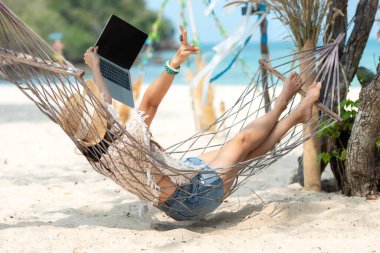 Hayat tarzı serbest çalışan bir kadın dizüstü bilgisayar kullanıyor ve sahilde rahatlıyor. Hamak başarısı olan Asyalı insanlar ve tatilde iş eğlenceleriniz ve internet konferansınızla birlikte. İş Yazı