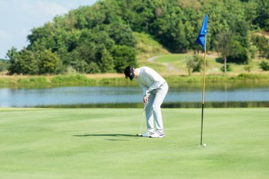 Golf oynayan golfçü yeşil sahada golf sopasıyla topu deliğe sokmayı hedefliyor. Profesyonel insanların tatilde hobisi ve güneşli bir sabahta golf kulübünde tatilleri. Yaşam Tarzı ve Spor Konsepti