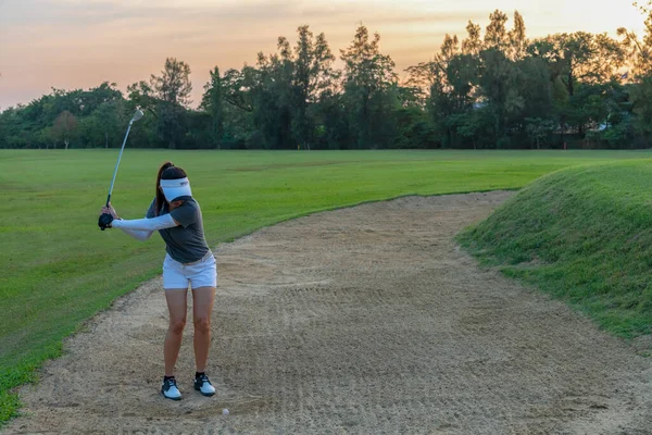 Golfer woman chip golf ball out of a sand trap. People swing and hitting golf course is on the fairway in sunset.  Hobby in holiday and vacations on club golf. Lifestyle and Sport Concept