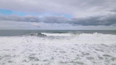 Parlak beyaz dalgaların ve bulutlu gökyüzünün görüntüsü.