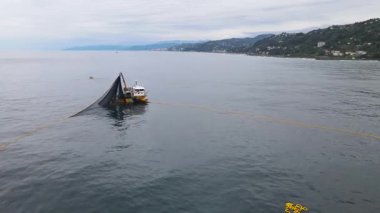 Ağlarını geri alan büyük bir balıkçı teknesinin kuş bakışı görüntüleri. Mavi sularda balıkçı teknesinde uçan kuşların olduğu etkileyici bir manzara..