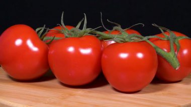 Siyah arkaplanda yeşil saplı kırmızı domateslerin yakın çekim görüntüleri.