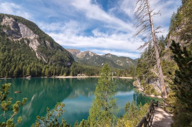 Orman dağlarına ve beyaz bulutlu mavi gökyüzüne karşı pürüzsüz turkuaz göl yüzeyi.