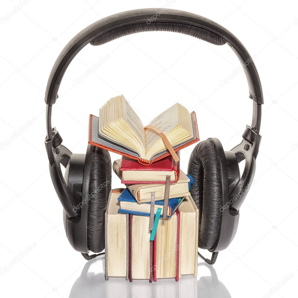 Stack of multicolored mini books and open book between ear pads of black headphones on isolated background