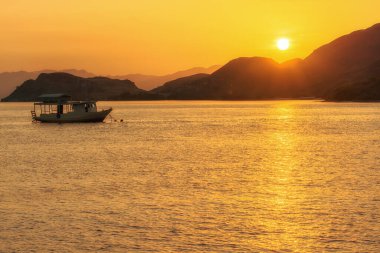 Tepe adalarının karanlık siluetleri gün batımında altın güneşin arka planında ve ön planda sakin suda bir tekne