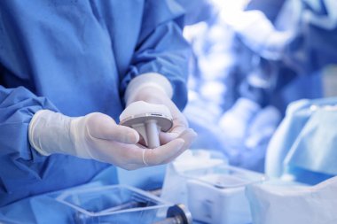 Eldivenli profesyonel, modern bir hastanede ortopedi ameliyatı için steril alana polietilen yerleştirilmiş diz protezi sunar..