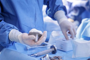 Eldivenli klinisyen, modern bir hastanede ortopedi ameliyatı sırasında steril bir alanda diz protezi bileşenleri hazırlıyor..