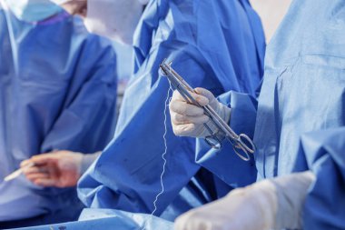 Eldivenli klinisyen steril ortopedik ameliyathanede iğne tutacağıyla dikiş atmaya hazırlanıyor. Eğitim, makale ve tıbbi cihaz için ideal..