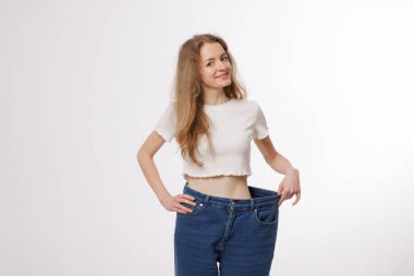 Gülümseyen kadın kilo verdikten sonra bol bol kot pantolon giyer. Dönüşüm sürecinde ilerleme kaydeder. Kendine güven ve sağlıklı bir hayat tarzı.