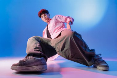 Sokak elbiseli düşük açılı Bboy. Stüdyoda mavi ışıklı poz veriyor.