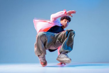 Breakdansçı, neon ışıklı bir stüdyoda düşük açılı dondurucu performans sergiliyor. Gençlik kültürü reklamları, müzik tanıtımları, posterler ve sosyal medya görselleri için mükemmel..