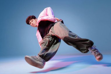 Hip hop dansçısı neon ışıklı bir stüdyoda dinamik ayak hareketleri yapıyor. Reklamlar, posterler ve gençlik kampanyaları için fotokopi alanı olan düşük açılı görüntüler sergiliyor..