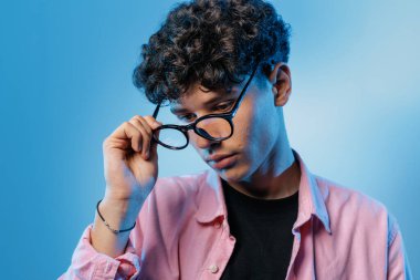 Genç, temiz bir stüdyo sahnesinde görme, reçete seçimi ve modern optometri eksikliği gösteren bir göz muayenesini düşünürken gözlükleri indiriyor..