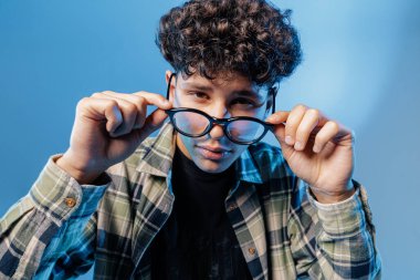 Genç kaldırma gözlüklerinin yakın portresi, kötü görüşü, modern optiği ve mavi bir stüdyonun arka planındaki göz bakımını gösteriyor.