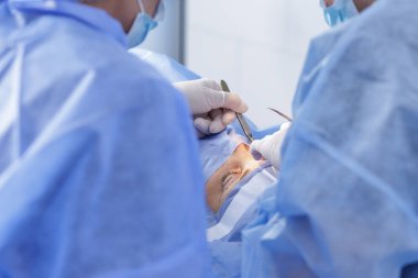 Eldiven cerrahları modern bir klinikte neşter ve forsepsle göz kapağı ameliyatı yaparlar.