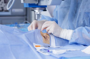 Eldivenli bir cerrah modern bir klinikte blefaroplasti yapmadan önce antiseptik uygularken işaretli bir göz kapağı üzerinde mikroskop ameliyat etmek