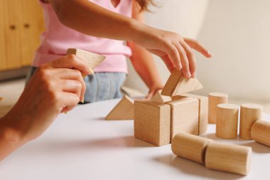 Ebeveyn, okul öncesi öğrenciye tahta bloklarla şekiller oluşturmasında yardımcı oluyor, oyun temelli öğrenme, iyi motor çalışması ve evde STEM hazırlığını gösteriyor