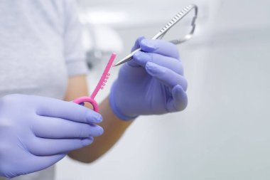 Steril bir diş kliniğindeki bir alete pembe elastik bir ip yükleyen bir klinisyenin kapatılması, diş tellerinin yerleştirme prosedürünü gösterir