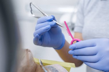 Eldivenli klinisyen, temiz bir klinikte diş tellerinin ayarlanmasını gösteren, dişçi aletli pembe elastik bir ip seçiyor.